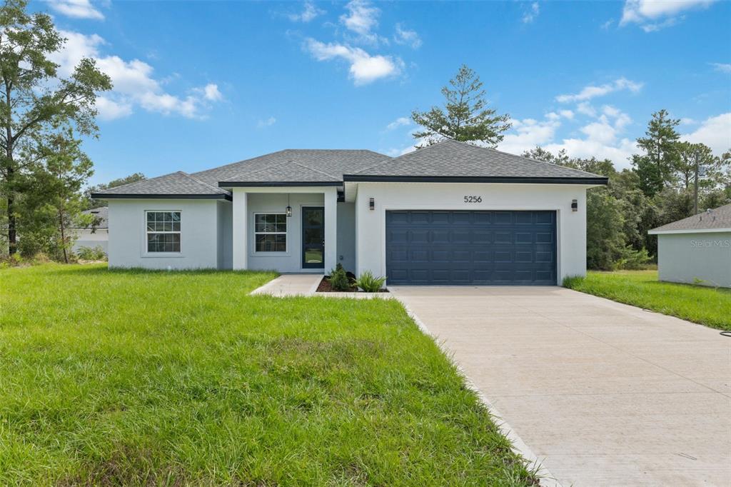 A single-story house with a white exterior, dark garage door, and a concrete driveway — 5256 SW 155TH LOOP, OCALA, FL