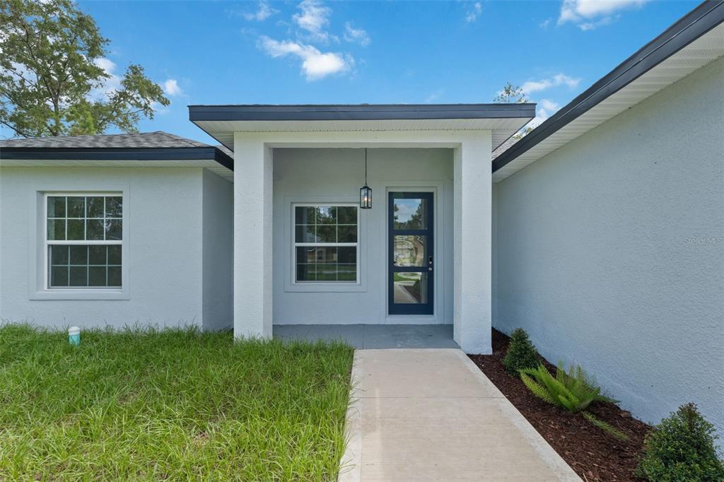 A concrete walkway leads to the covered front entrance of a light-colored house — 5256 SW 155TH LOOP, OCALA, FL