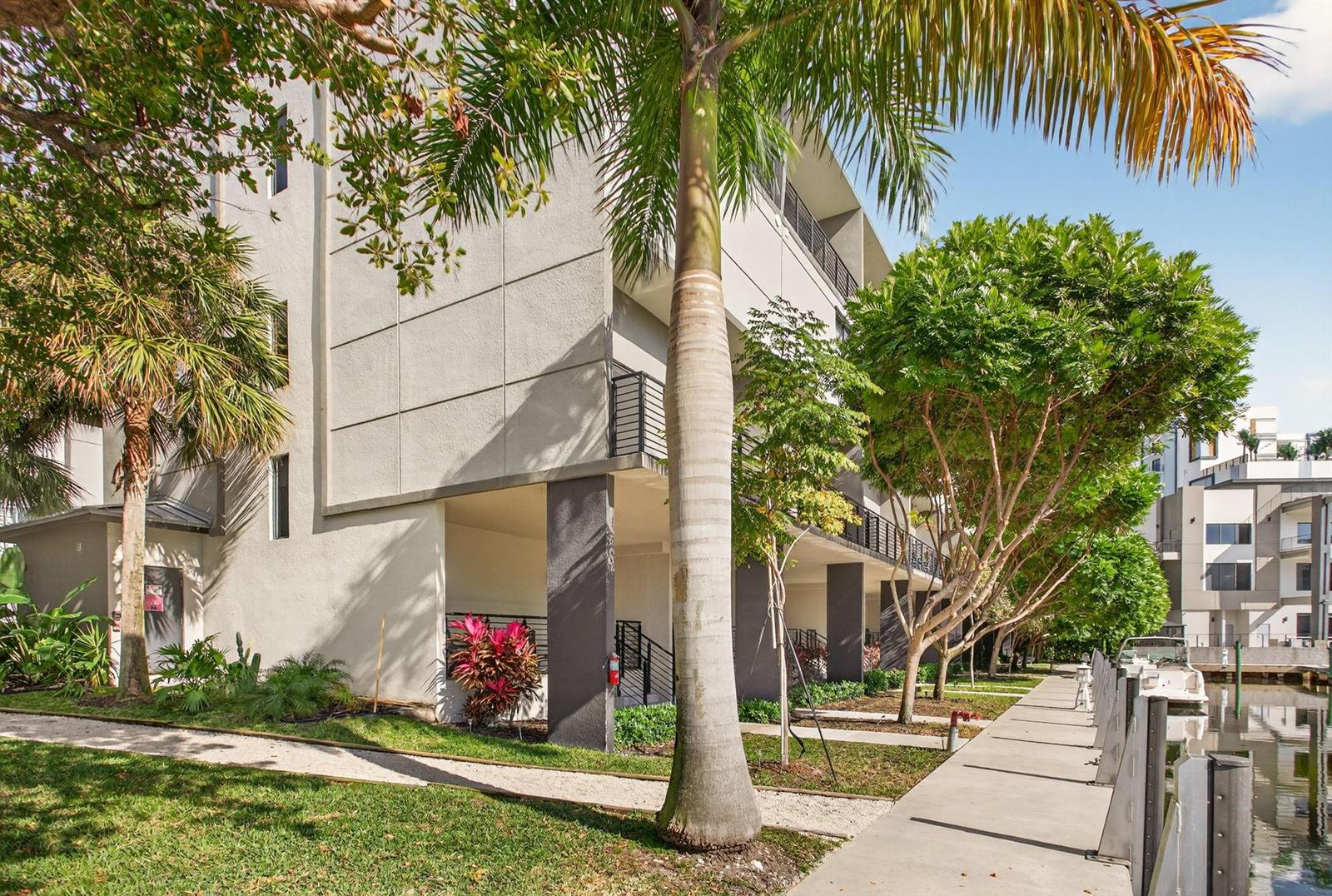 Exterior view of a multi-story apartment building with a palm tree and a canal walkway — 196 SE 4th Terrace # 1, Pompano Beach FL 33060, POMPANO BEACH, FL
