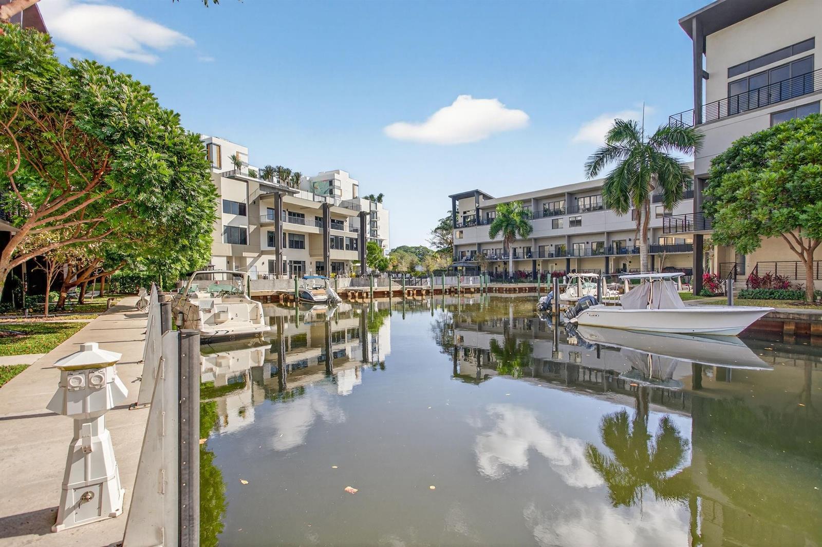 A canal with docked boats sits between two modern multi-story residential buildings under a blue sky — 196 SE 4th Terrace # 1, Pompano Beach FL 33060, POMPANO BEACH, FL