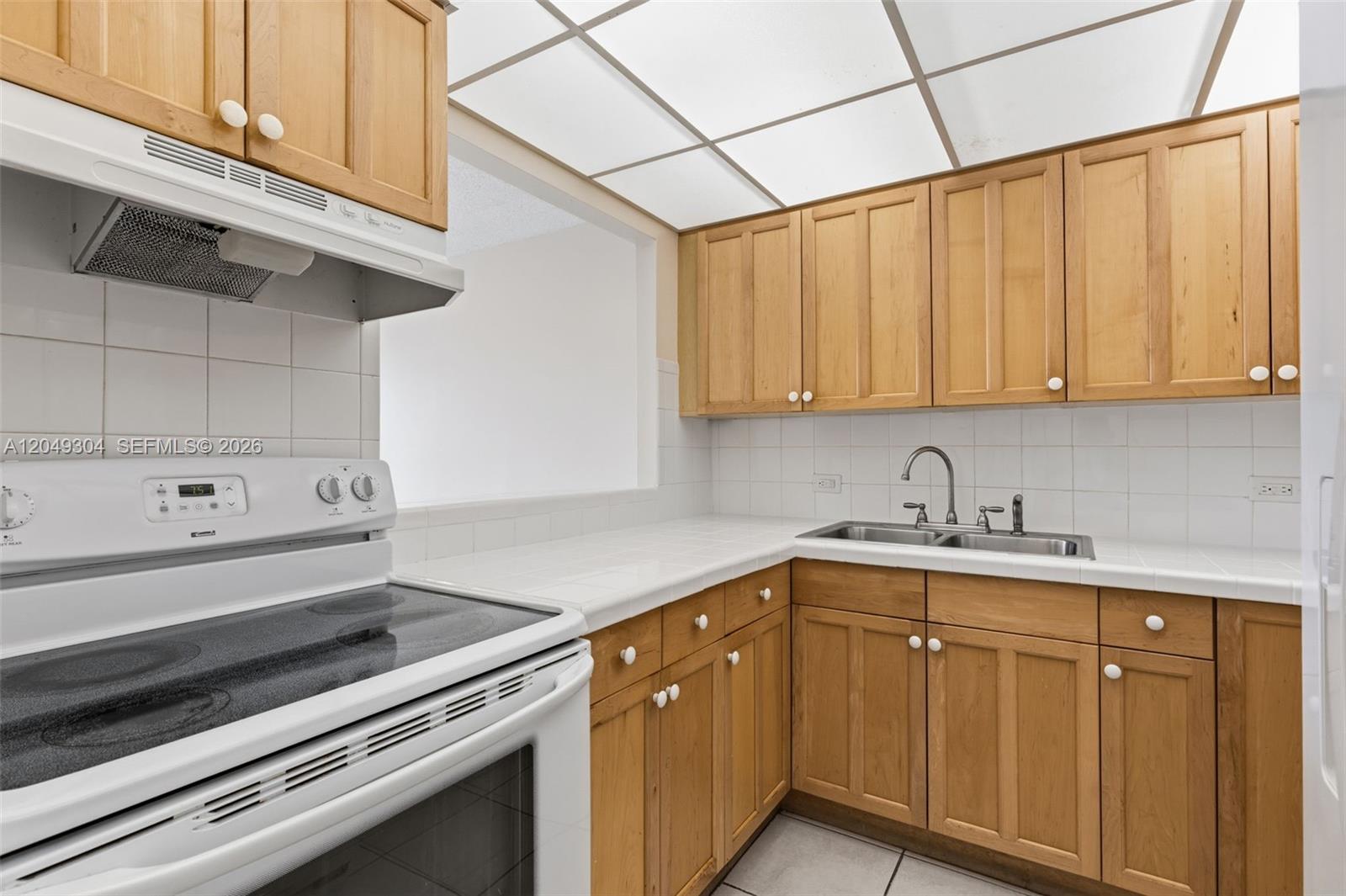 A kitchen features light wood cabinets, white tiled countertops, and a white electric stove — 10425 SW 112th Ave # 302, Miami FL 33176, MIAMI, FL