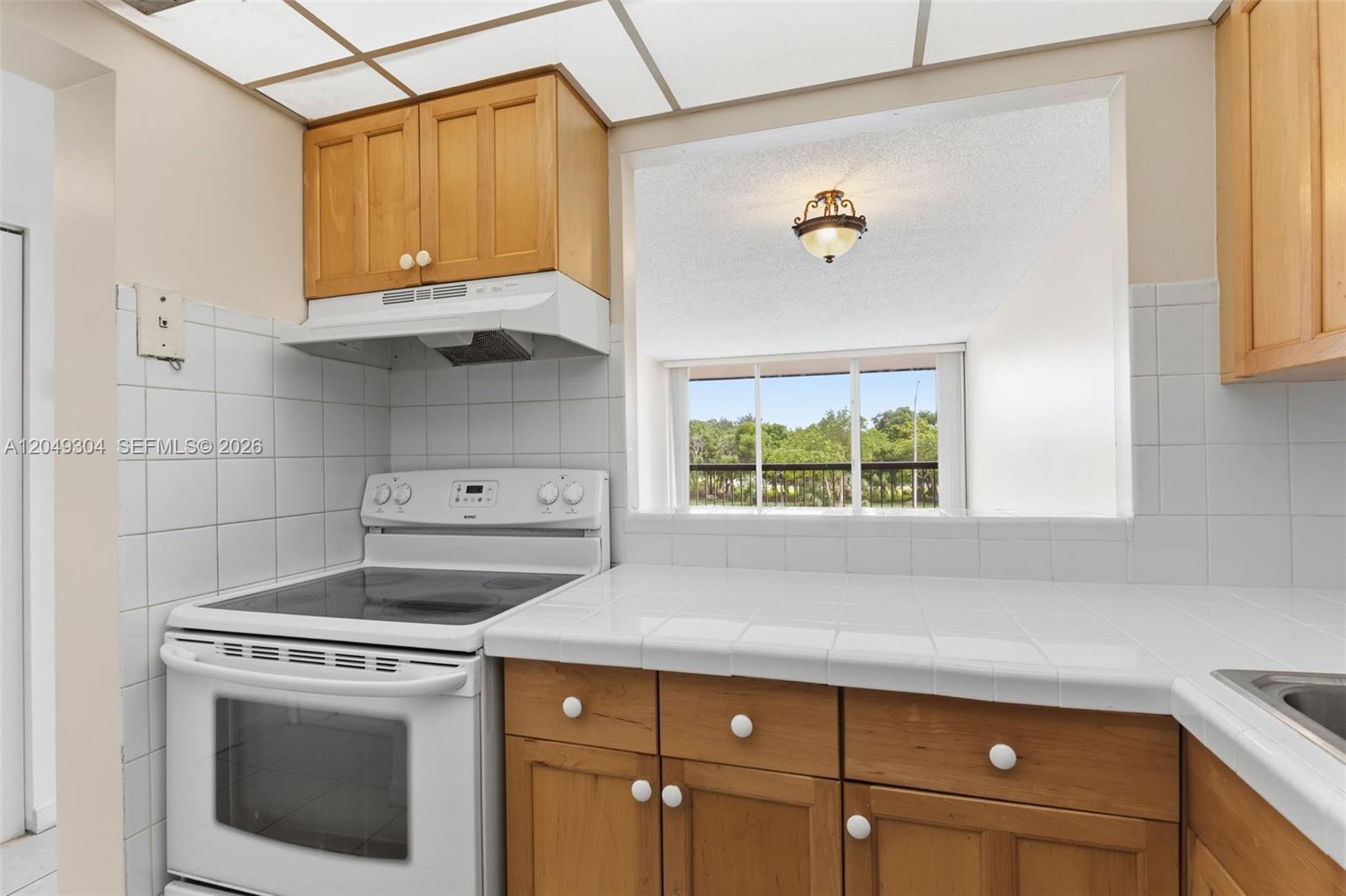A kitchen features wood cabinets, white tile countertops, a white electric stove, and a window — 10425 SW 112th Ave # 302, Miami FL 33176, MIAMI, FL