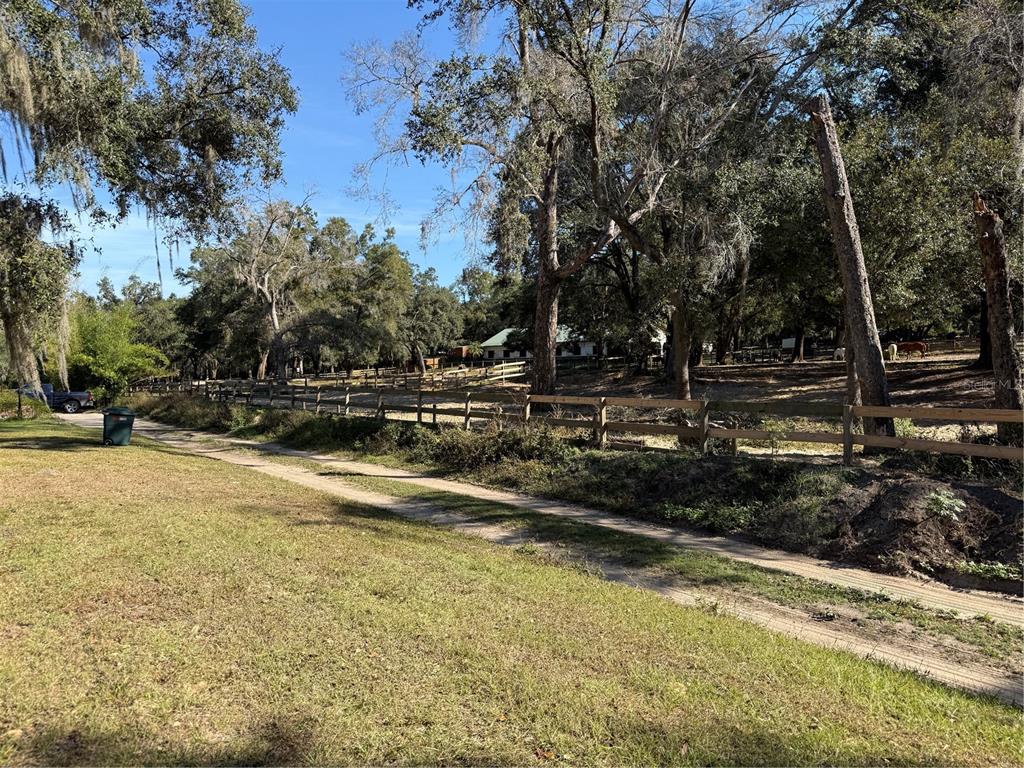 A dirt path runs alongside a wooden fence bordering a grassy field with mature trees — TRACT 6 WOODY LANE, DADE CITY, FL
