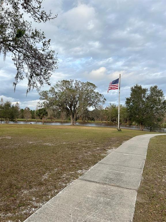A paved walkway leads toward a grassy field with a pond and an American flag — 107 HIBISCUS DRIVE, INDIAN LAKE ESTATES, FL