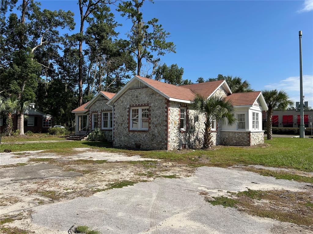 A stone-clad house with a brown roof sits on a lot with a paved area — 1008 NW 13TH STREET, GAINESVILLE, FL
