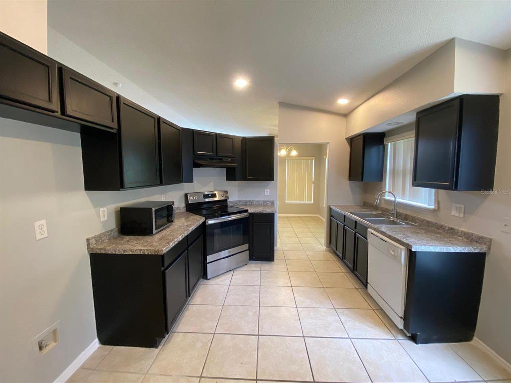 A kitchen features dark cabinets, stainless steel appliances, laminate countertops, and light-colored floor tiles — 1440 TIMBERBEND CIRCLE, ORLANDO, FL