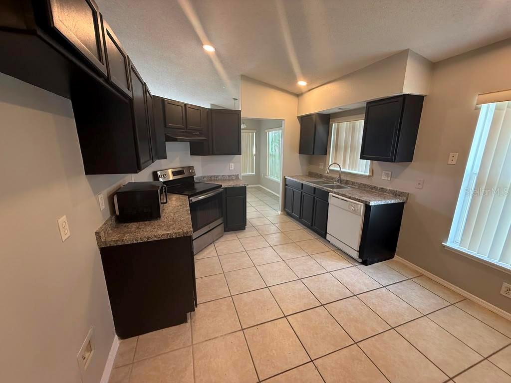A kitchen features dark cabinets, granite countertops, stainless steel appliances, and light-colored tile flooring — 1440 TIMBERBEND CIRCLE, ORLANDO, FL