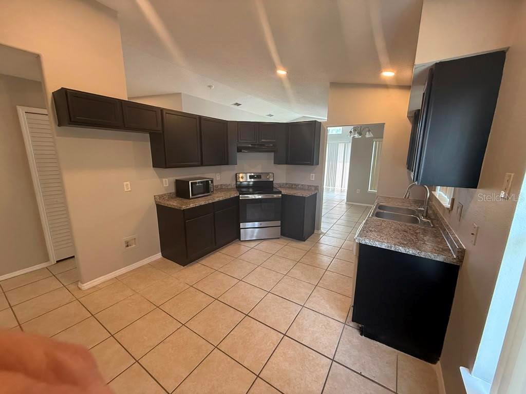A kitchen features dark wood cabinets, laminate countertops, stainless steel appliances, and tiled flooring — 1440 TIMBERBEND CIRCLE, ORLANDO, FL