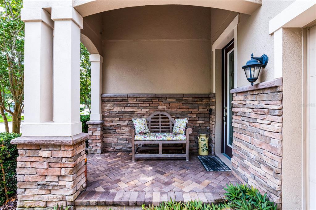 A covered front porch features a stone facade, a wooden bench, and brick pavers — 14413 MAGNOLIA RIDGE LOOP, WINTER GARDEN, FL