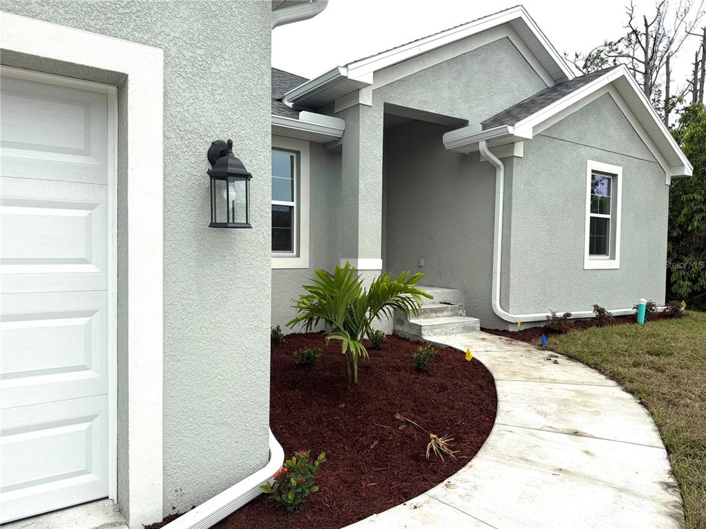 A view of a house exterior featuring a garage, walkway, and landscaped mulch bed — 9590 LITTLE ROCK STREET, PORT CHARLOTTE, FL