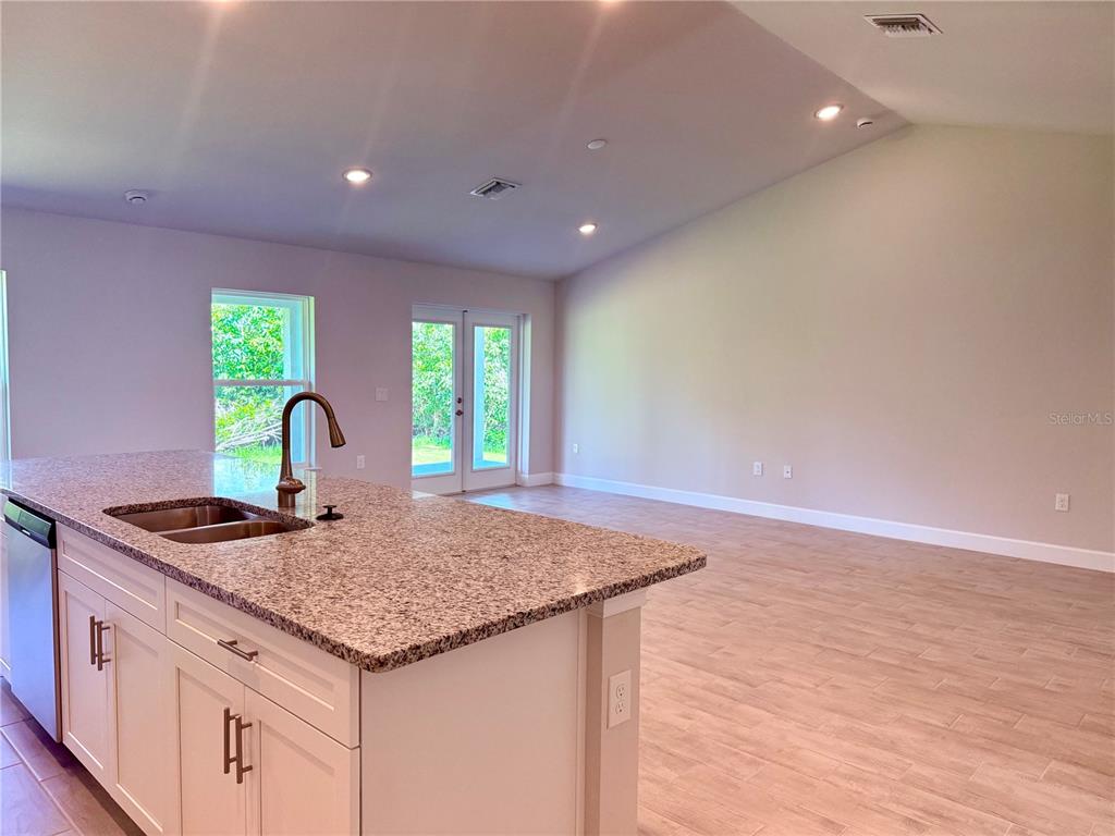 A kitchen island with a granite countertop and sink overlooks an open living area — 9590 LITTLE ROCK STREET, PORT CHARLOTTE, FL