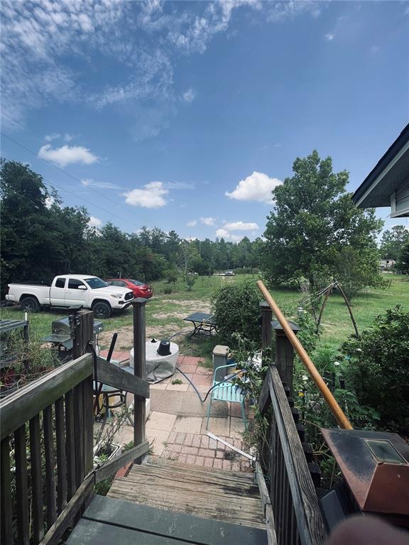 A wooden staircase leads down to a paved patio area with a yard and parked vehicles — 16570 SW 58TH LANE, OCALA, FL