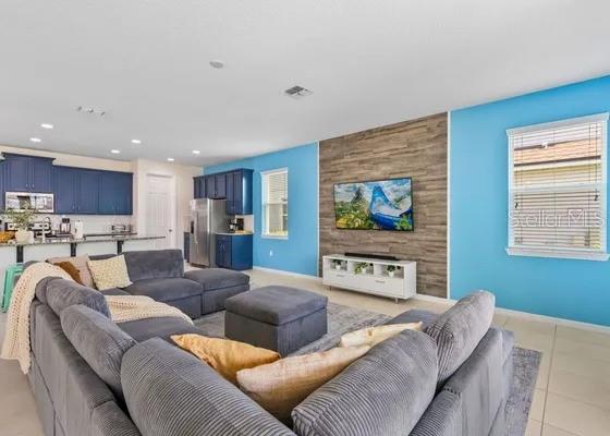 A living room with a gray sectional sofa, blue walls, and a wood-paneled accent wall — 9042 SUNSHINE RIDGE LOOP, KISSIMMEE, FL