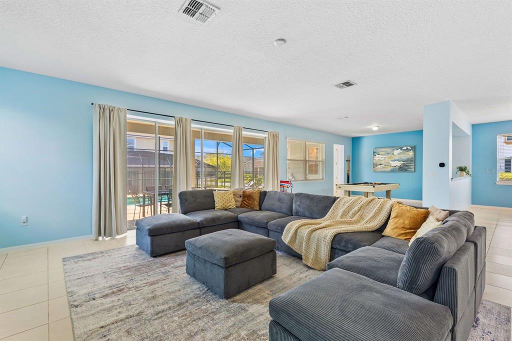 A living room features a large gray sectional sofa, a matching ottoman, and a pool view — 9042 SUNSHINE RIDGE LOOP, KISSIMMEE, FL
