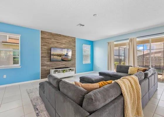 A living room features light blue walls, a wood-paneled accent wall, and a large sectional sofa — 9042 SUNSHINE RIDGE LOOP, KISSIMMEE, FL
