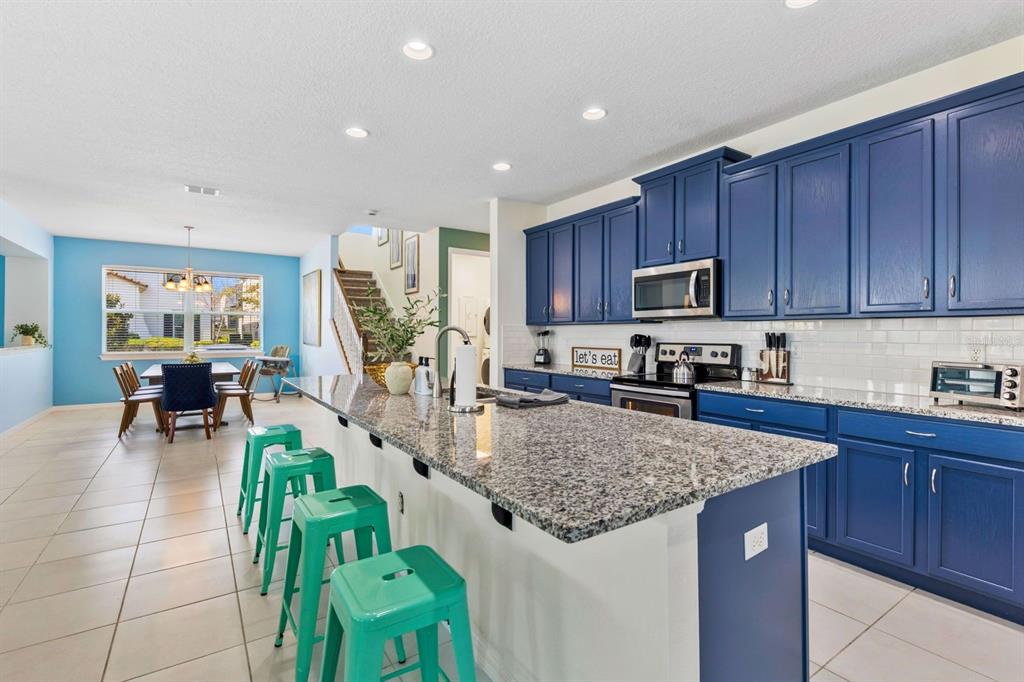 A kitchen with blue cabinets, granite countertops, and a breakfast bar with teal stools — 9042 SUNSHINE RIDGE LOOP, KISSIMMEE, FL