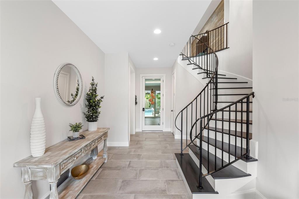 A foyer features a curved staircase with black railings, tile flooring, and a wooden console — 124 FOREST HILLS DRIVE, REDINGTON SHORES, FL