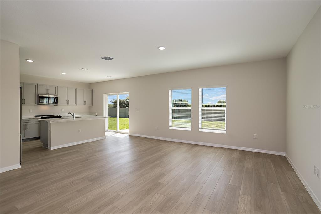 An open-concept kitchen and living area features light gray cabinetry, wood-look flooring, and sliding doors — 6055 PRAIRIE RUN, HAINES CITY, FL