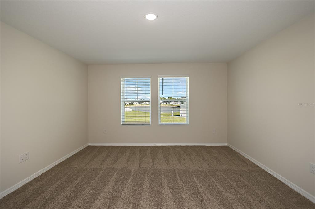 An empty bedroom features beige walls, tan carpeting, and two windows overlooking a grassy area — 6055 PRAIRIE RUN, HAINES CITY, FL