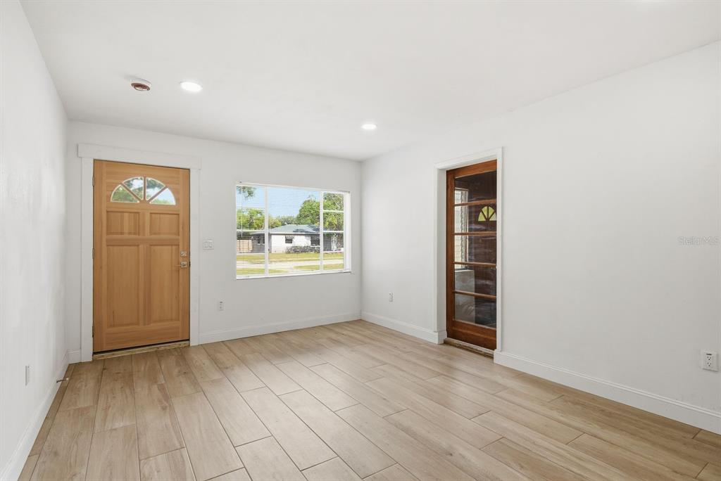 An empty room features light wood-look tile flooring, white walls, a wooden front door, and a window — 4325 S COOLIDGE AVENUE, TAMPA, FL