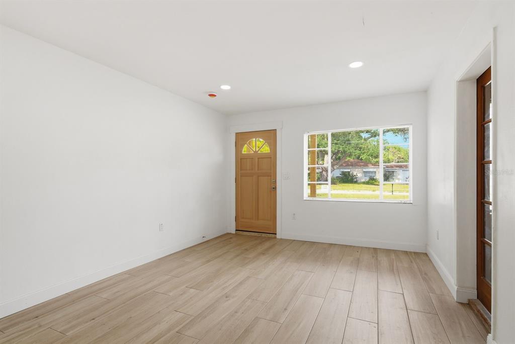 An empty room with light wood-look tile flooring, white walls, a wooden front door, and windows — 4325 S COOLIDGE AVENUE, TAMPA, FL