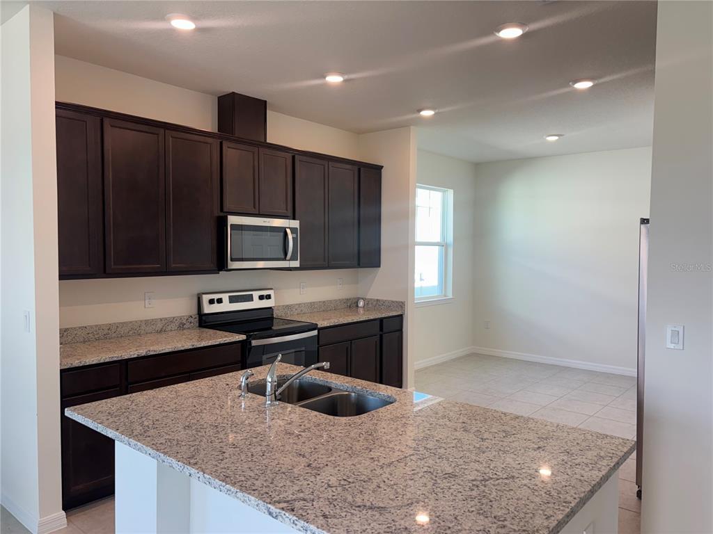 A kitchen features dark wood cabinets, granite countertops, a center island, and stainless steel appliances — 2355 SELENIA STREET, LAKE ALFRED, FL