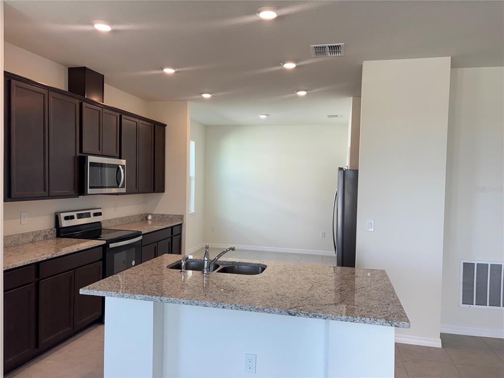 A kitchen features dark wood cabinets, granite countertops, a center island, and stainless steel appliances — 2355 SELENIA STREET, LAKE ALFRED, FL