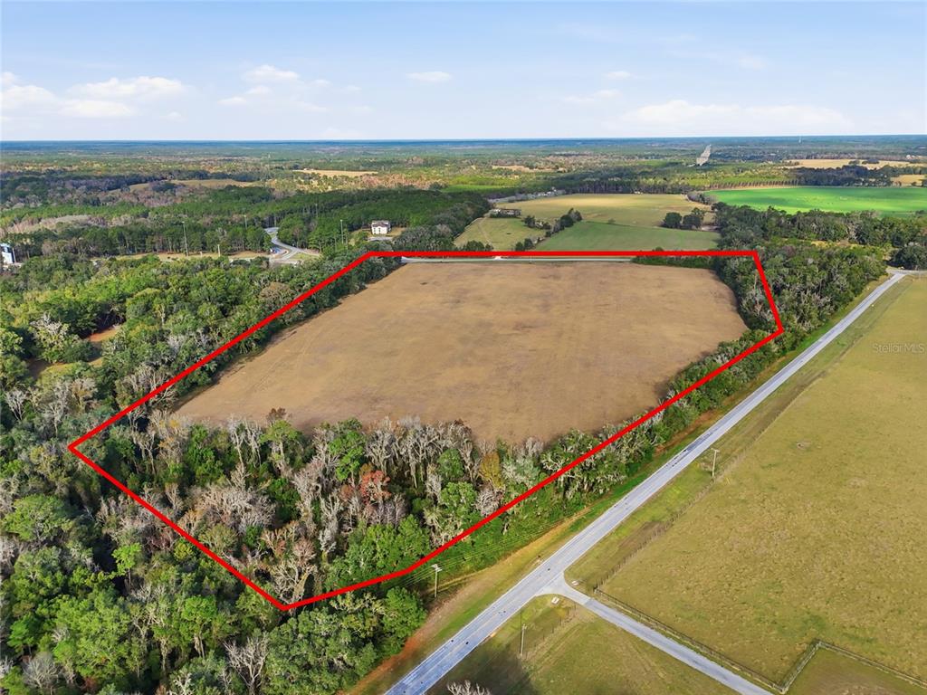 An aerial view shows a large, cleared rectangular field surrounded by dense forest and trees — Hwy 236 NW 236, ALACHUA, FL
