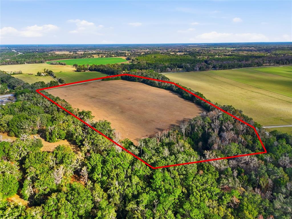 An aerial view shows a large, cleared rectangular field surrounded by dense green forest — Hwy 236 NW 236, ALACHUA, FL