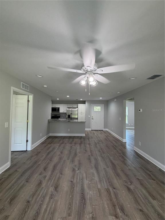 An open-concept living area features gray walls, wood-look flooring, a ceiling fan, and a kitchen — 1981 LEMON DRIVE, LAKE WALES, FL