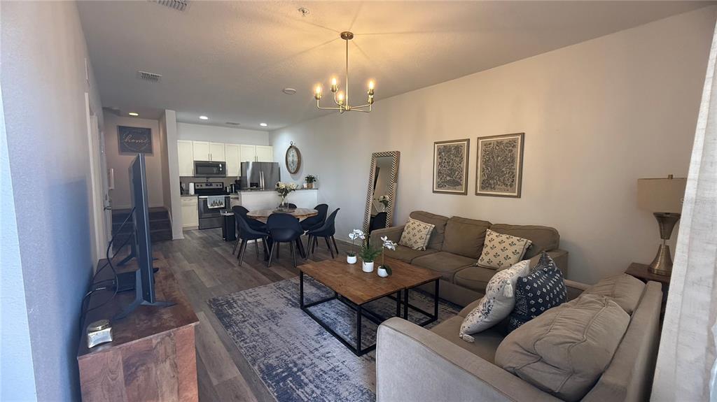 An open-concept living and dining area features wood-look flooring, a chandelier, and neutral furniture — 8919 SHINE DRIVE, KISSIMMEE, FL