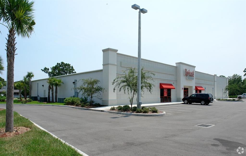 A commercial building with a parking lot, palm trees, and red awnings under a clear sky — 311 S RIDGEWOOD AVENUE, EDGEWATER, FL