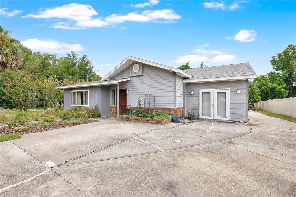 A gray, single-story house with a concrete driveway, brick planter, and double glass doors — 1420 E 8TH AVENUE, MOUNT DORA, FL