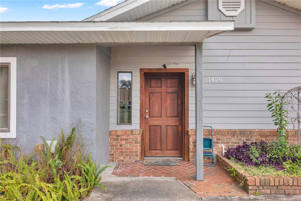 A front entrance features a wooden door, brick porch, and gray horizontal siding — 1420 E 8TH AVENUE, MOUNT DORA, FL