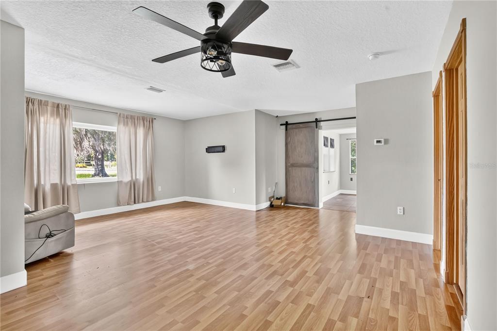 A living room features light wood-look flooring, gray walls, a ceiling fan, and a barn door — 1420 E 8TH AVENUE, MOUNT DORA, FL