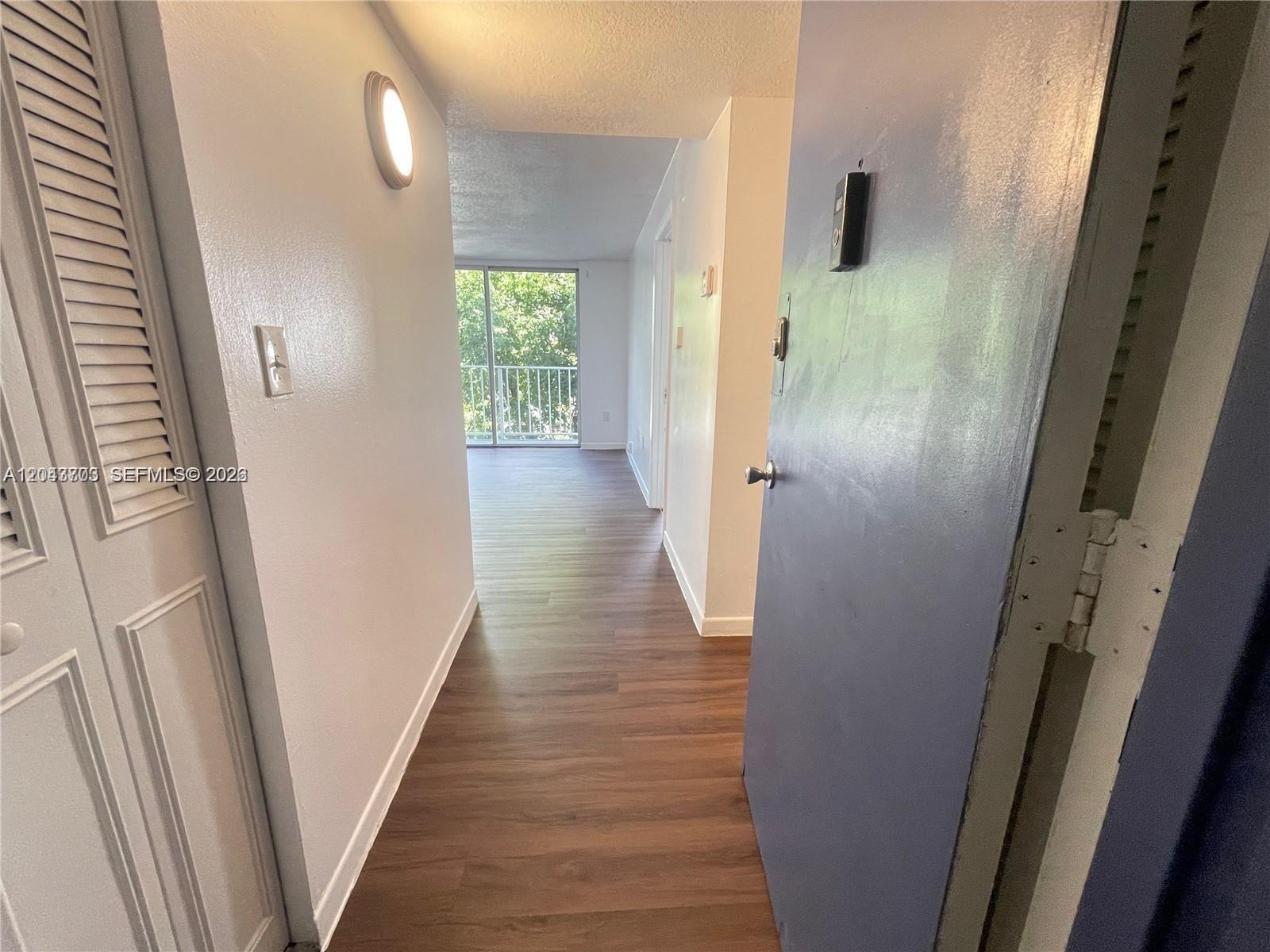 A hallway with wood-look flooring leads toward a balcony with a view of trees — 1740 NW N River Dr # 517, Miami FL 33125, MIAMI, FL