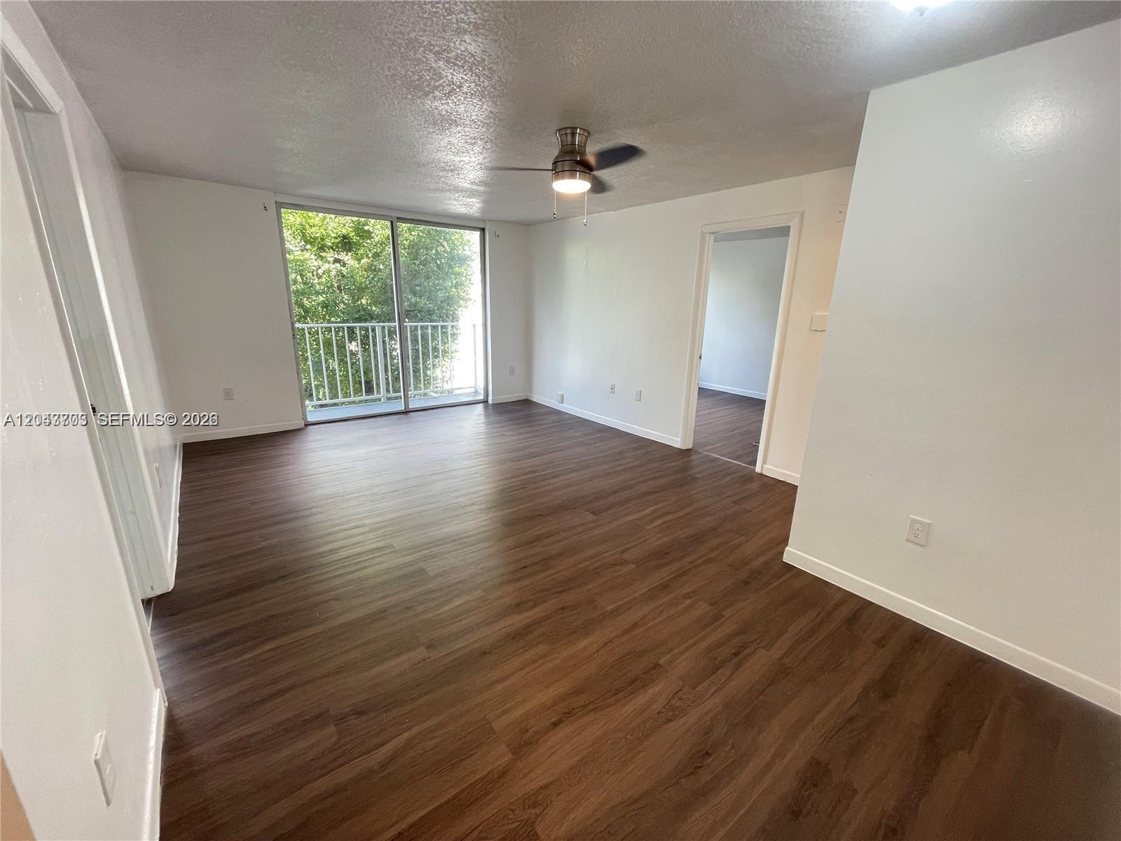 An empty room features wood-look flooring, a ceiling fan, and a sliding glass door — 1740 NW N River Dr # 517, Miami FL 33125, MIAMI, FL