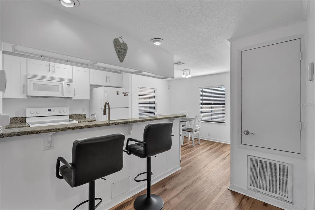 A kitchen features white cabinets, a granite breakfast bar with two stools, and wood flooring — 373 ERON WAY UNIT 47, WINTER GARDEN, FL