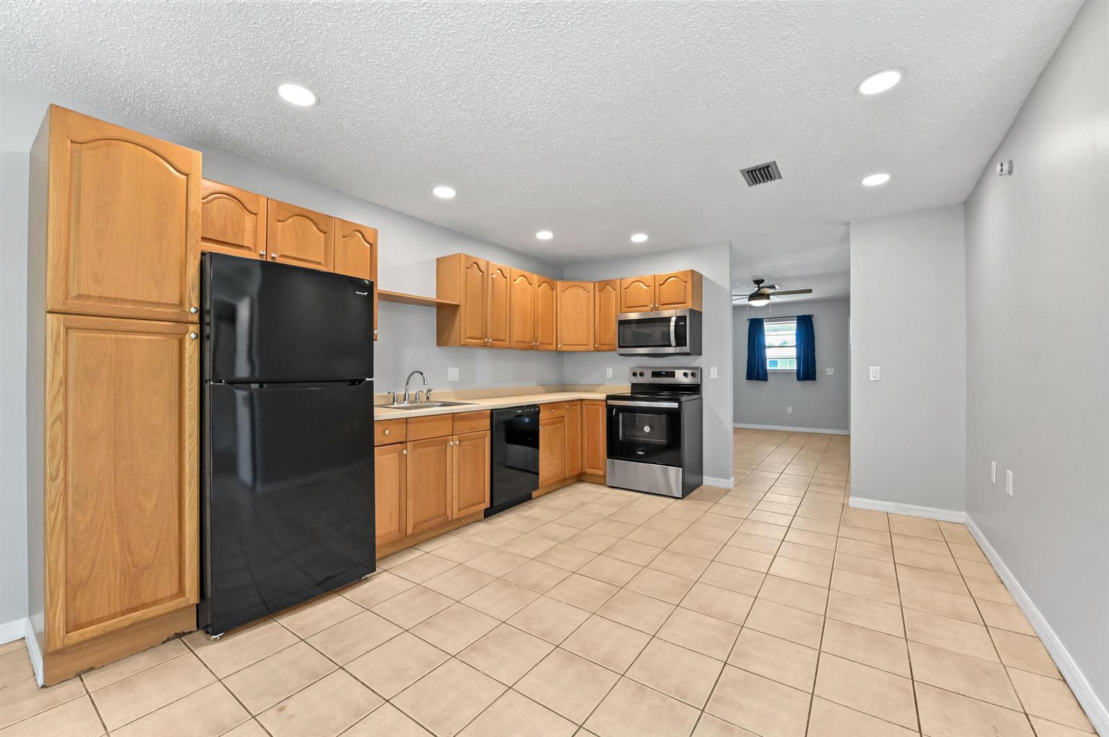 A kitchen features wood cabinets, black and stainless appliances, and light-colored tile flooring — 4550 SE Salvatori Road, Stuart FL 34997, STUART, FL