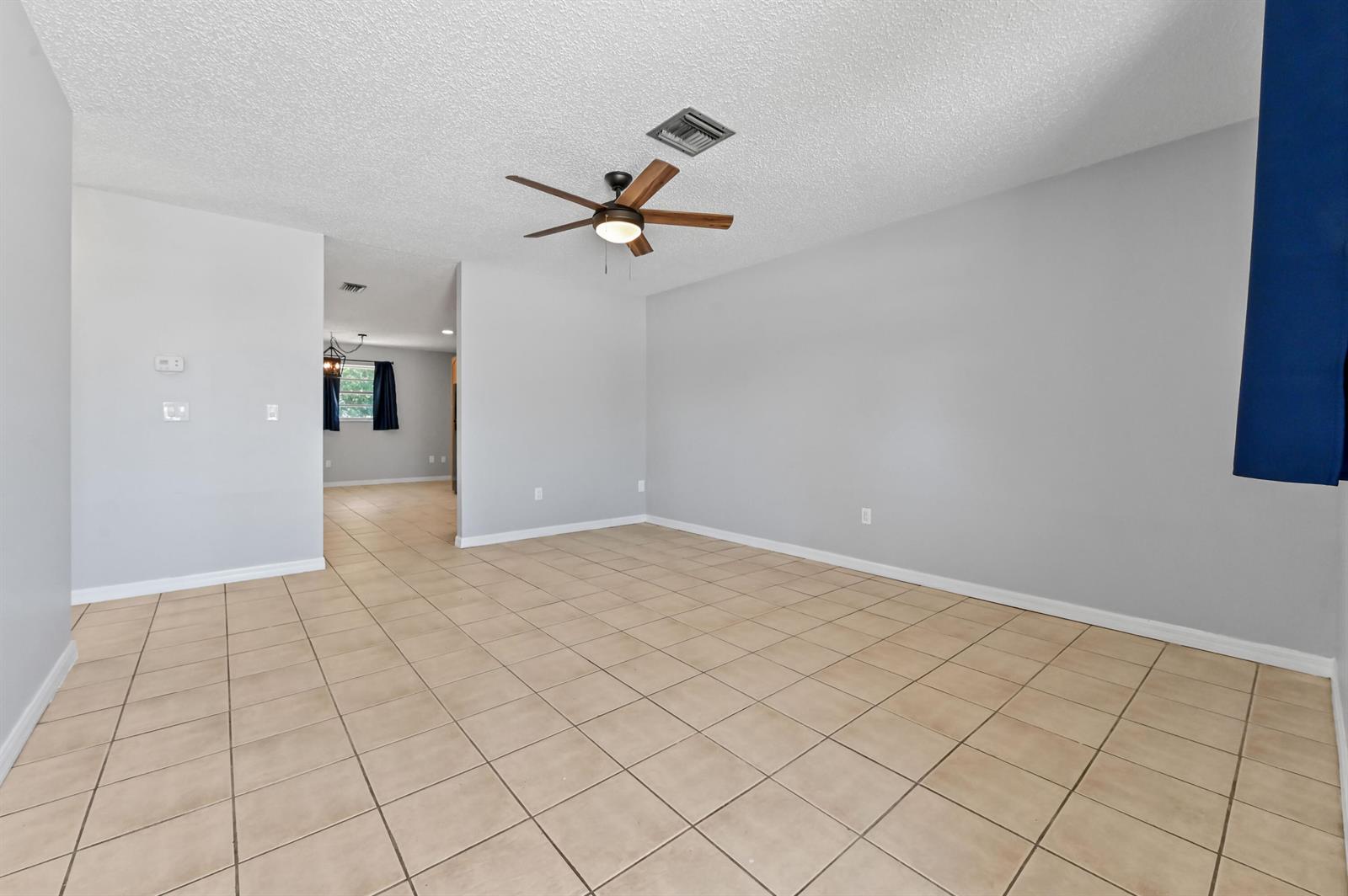An empty living room features light gray walls, beige tile flooring, and a ceiling fan — 4550 SE Salvatori Road, Stuart FL 34997, STUART, FL