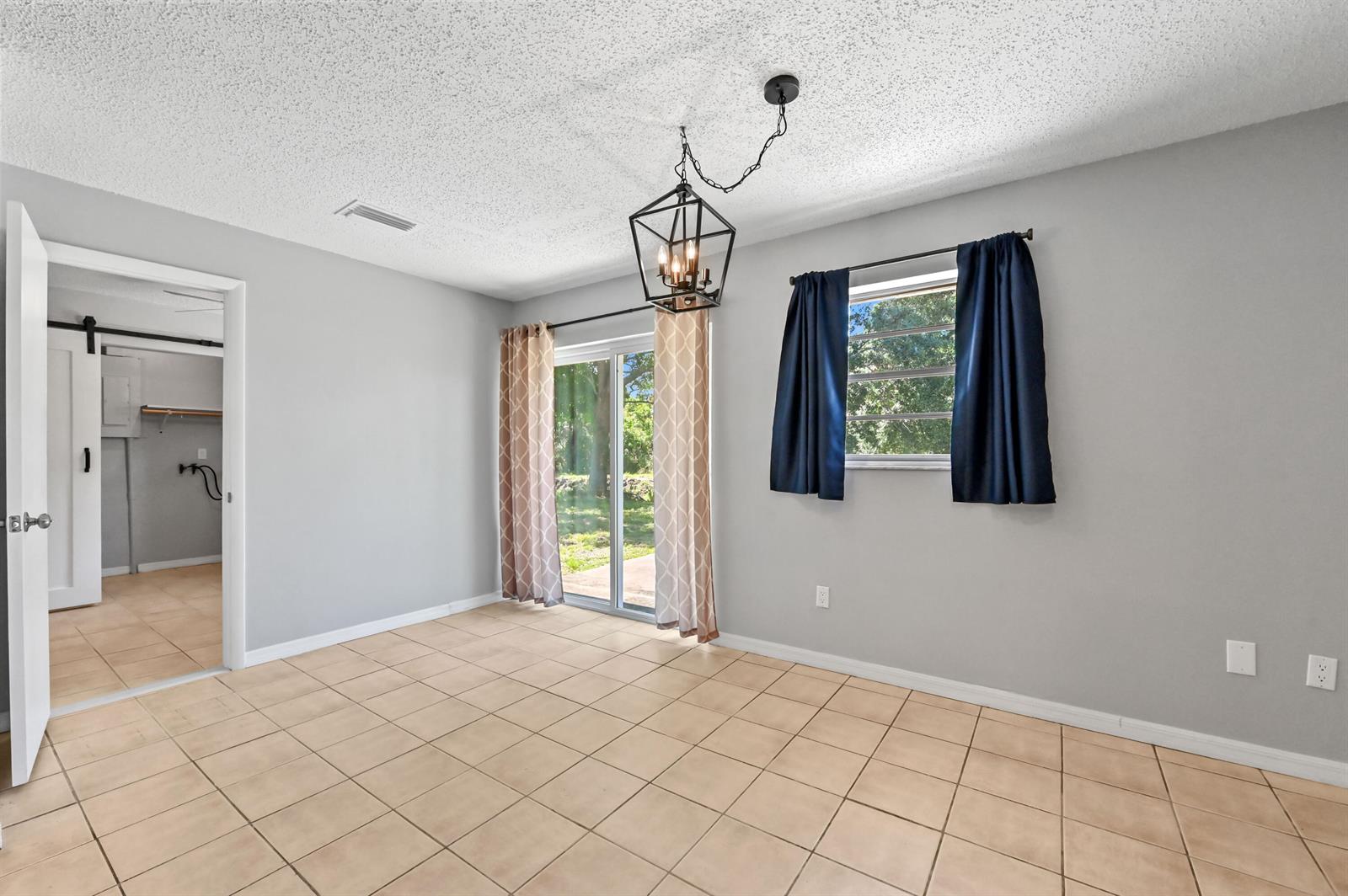 A room with light gray walls, tile flooring, a sliding glass door, and a chandelier — 4550 SE Salvatori Road, Stuart FL 34997, STUART, FL