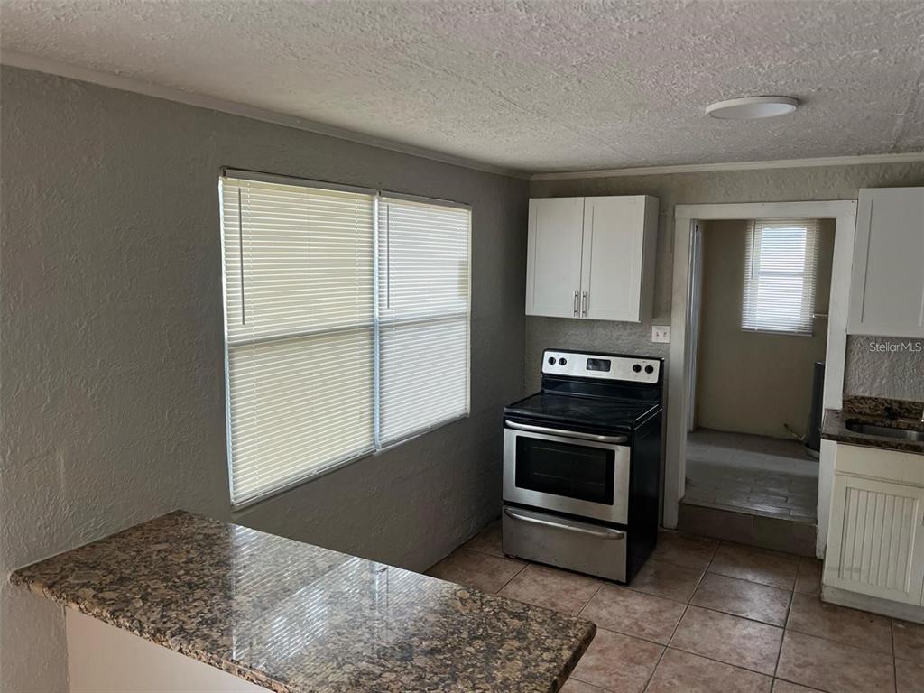 A kitchen features a granite countertop, a black stove, white cabinets, and tiled flooring — 1450 WAKULLA WAY, ORLANDO, FL