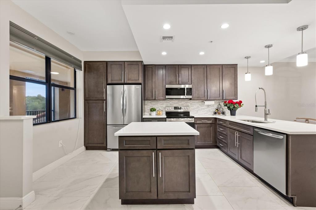 A modern kitchen features dark wood cabinets, white countertops, a central island, and stainless appliances — 16300 COUNTY ROAD 455 UNIT 204, MONTVERDE, FL