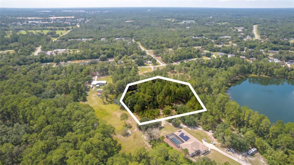 An aerial view shows a wooded lot outlined in white next to a large lake — 3106 SAINT JAMES AVENUE, DELTONA, FL