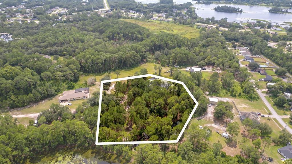 An aerial view shows a wooded, pentagonal-shaped plot of land surrounded by residential properties — 3106 SAINT JAMES AVENUE, DELTONA, FL