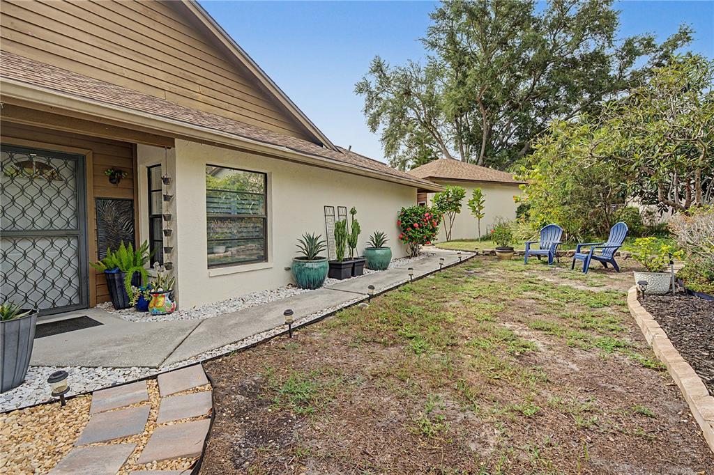 A side view of a house exterior featuring a concrete walkway, potted plants, and lawn — 207 LIGHTHOUSE COURT, SAFETY HARBOR, FL