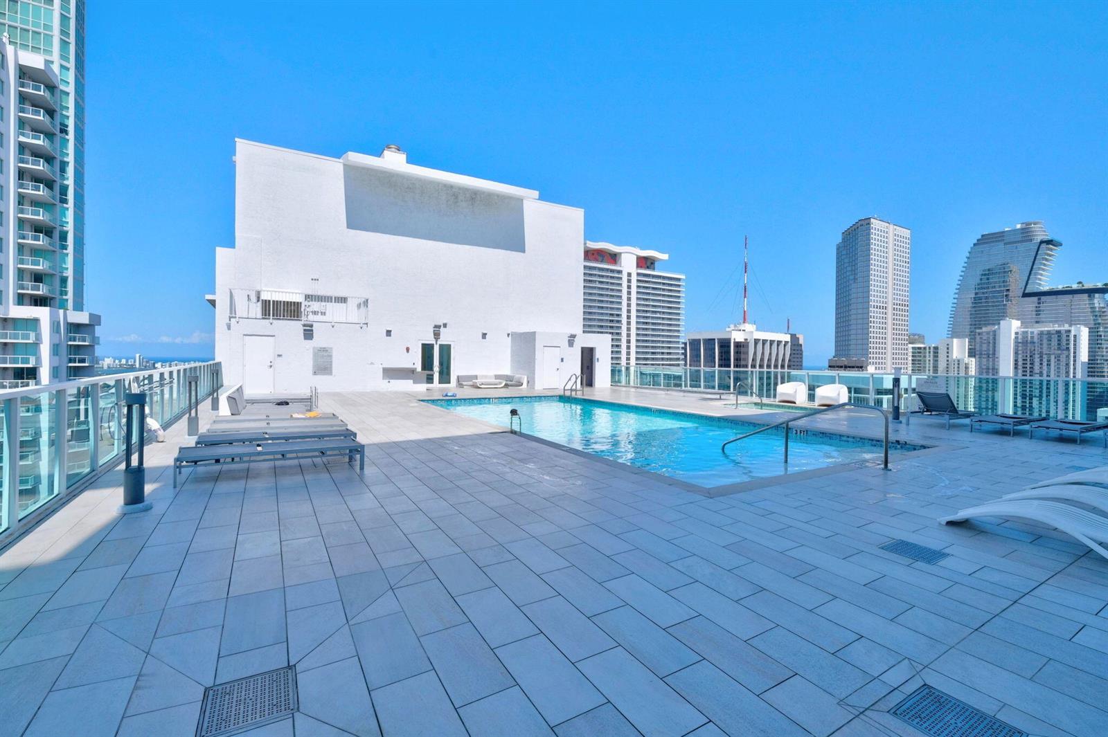 A rooftop swimming pool surrounded by lounge chairs on a tiled deck with city views — 133 NE 2nd Avenue # 1408, Miami FL 33132, MIAMI, FL