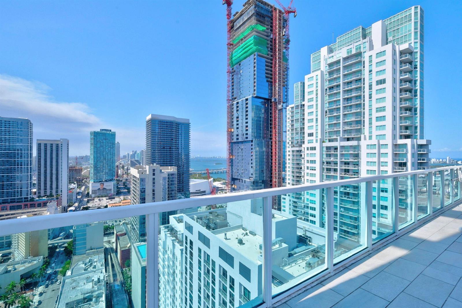 A high-rise balcony overlooks a dense urban cityscape with several skyscrapers and a distant bay — 133 NE 2nd Avenue # 1408, Miami FL 33132, MIAMI, FL