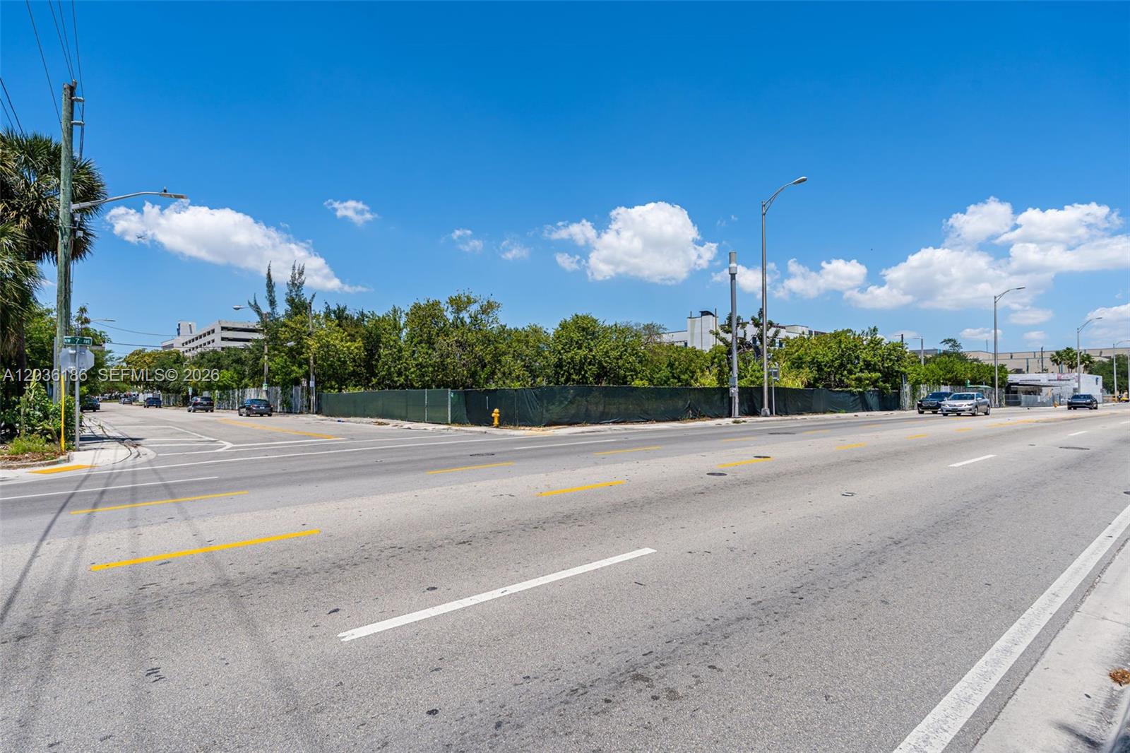 A vacant, fenced-in corner lot sits at a paved intersection under a clear blue sky — 1800 NW 7th Ave, Miami FL 33136, MIAMI, FL