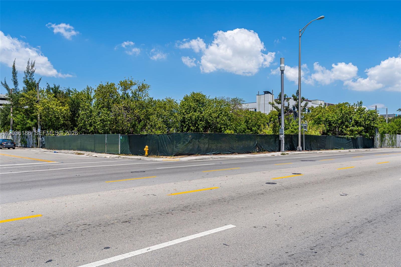 A fenced, vacant corner lot sits beside a paved road under a blue sky — 1800 NW 7th Ave, Miami FL 33136, MIAMI, FL
